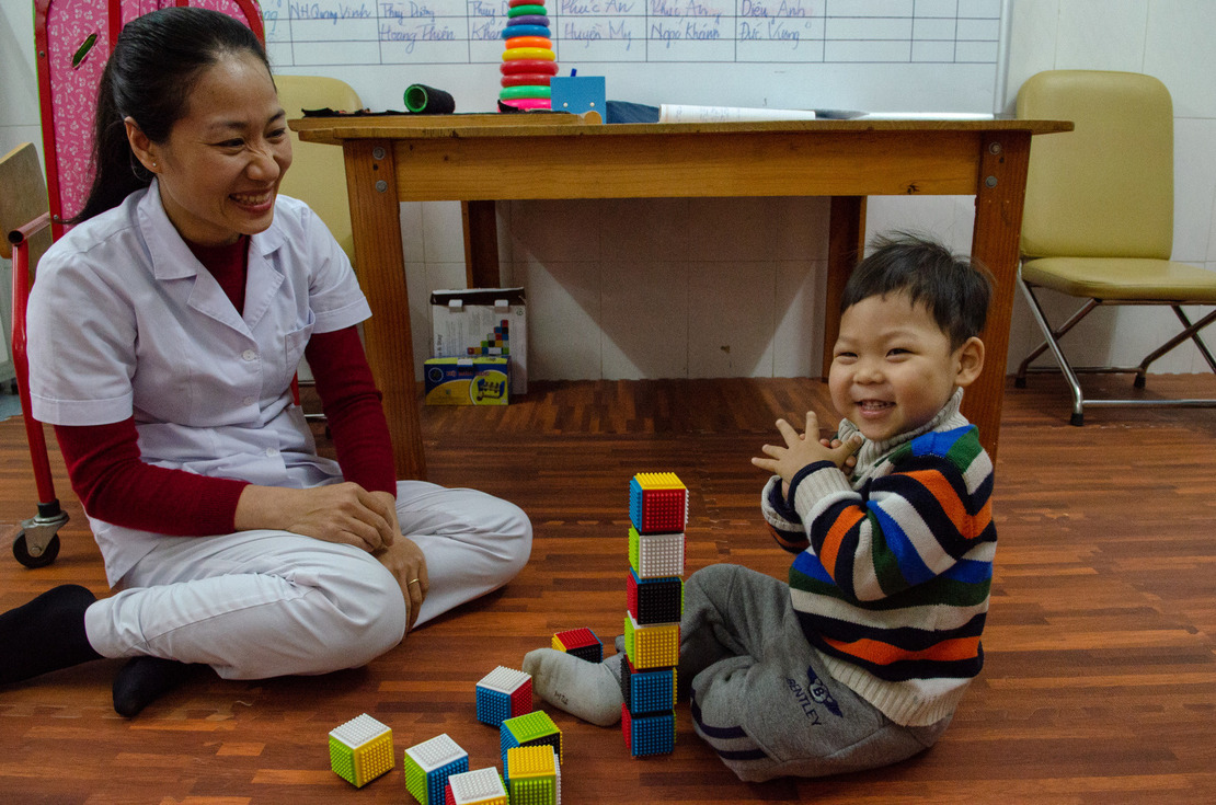 A little boy is applauding because he managed to build a tower with cubes in front of HI occupationnal therapist.